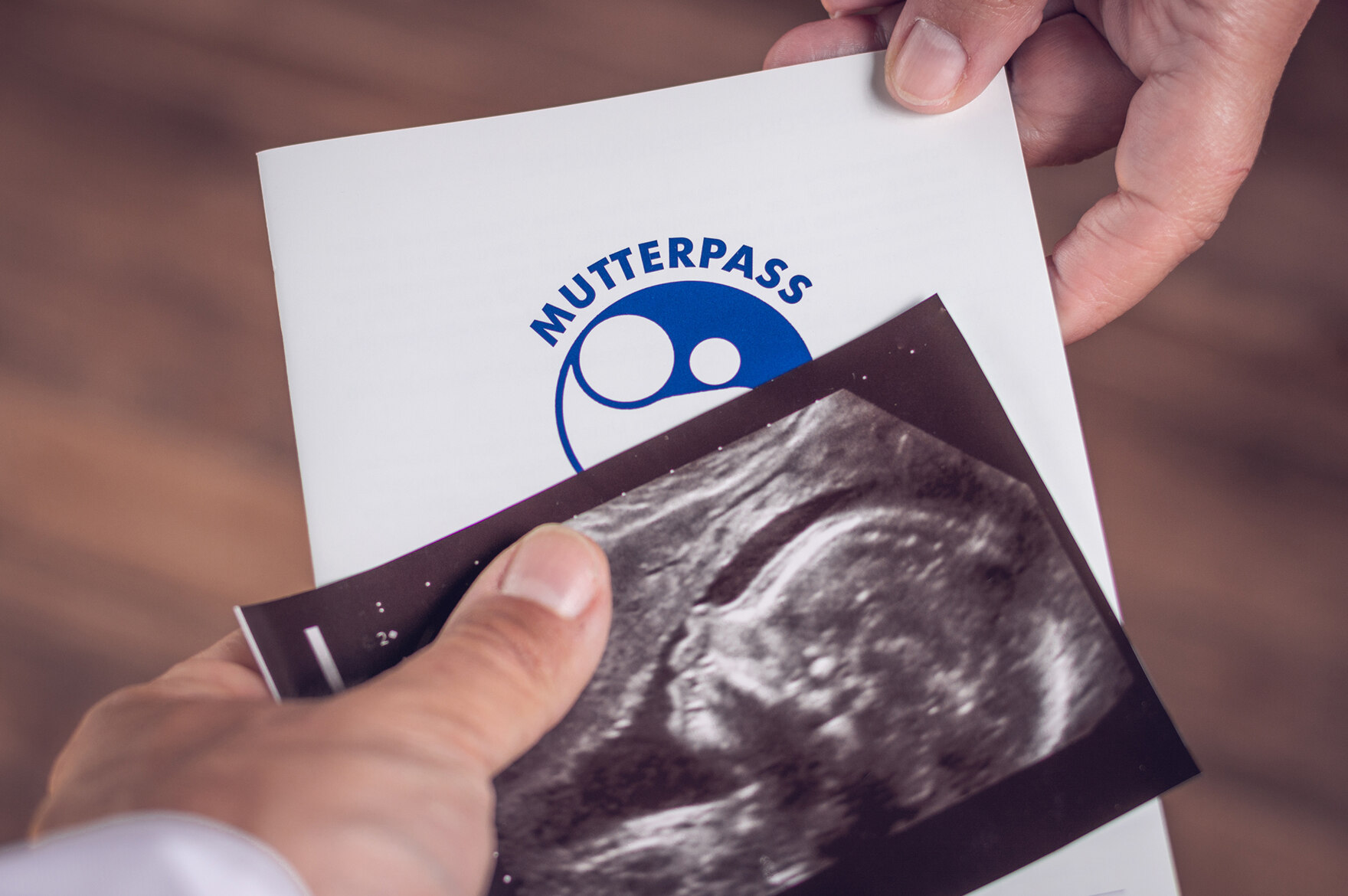 Mutterpass und Ultraschallbild werden von einer Hand in eine andere weitergereicht