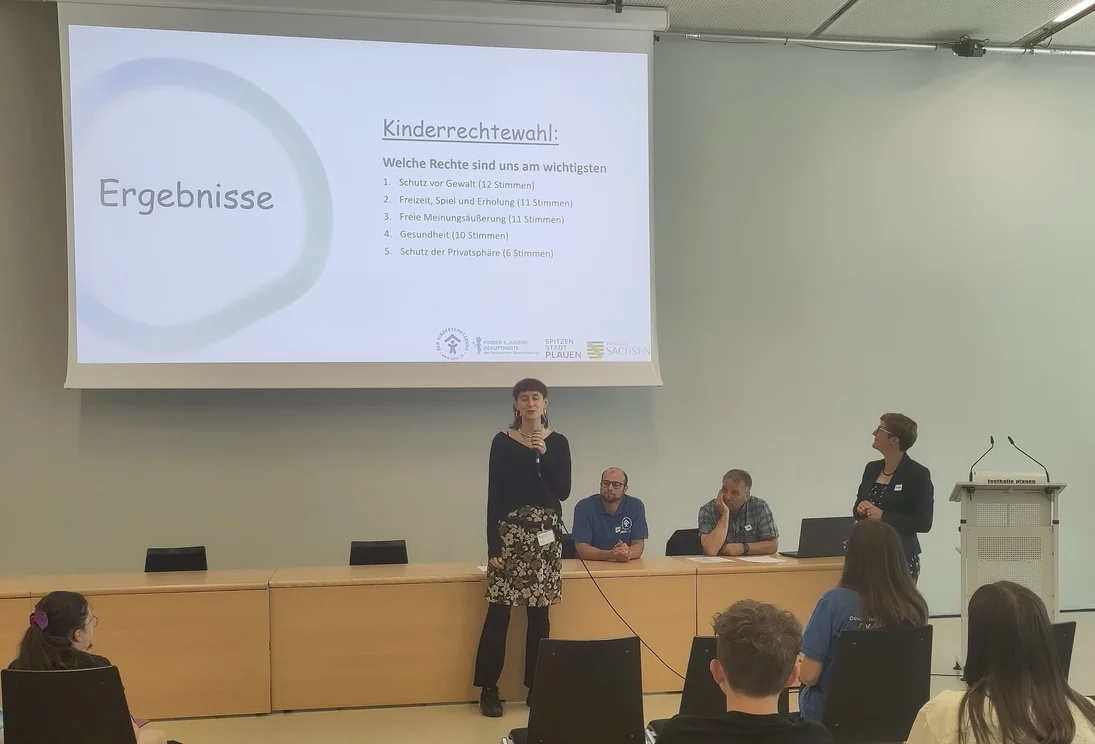 Person spricht vor Publikum. Im Hintergrund eine Leinwand mit dem Wort Kinderrechtewahl