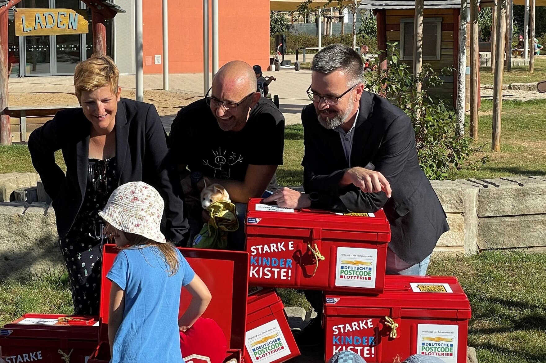 Drei Menschen hinter gespalten kleine roten Kisten. Auf den Kisten steht Starke Kinder Kisten