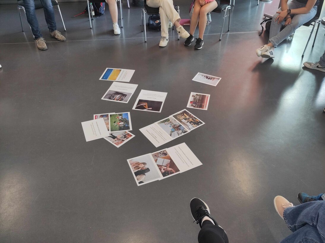 Füße im Stuhkreis. Auf dem Boden liegen bunte Bilder und Karten mit kurzen Texten der Kinderrechte