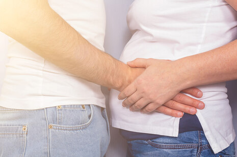 Ein Mann hält einer schwangeren Frau den Bauch, sie fasst seine Hand an