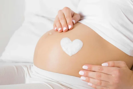Schwangere Frau. Auf dem Bauch ist ein weißes Herz gelegt