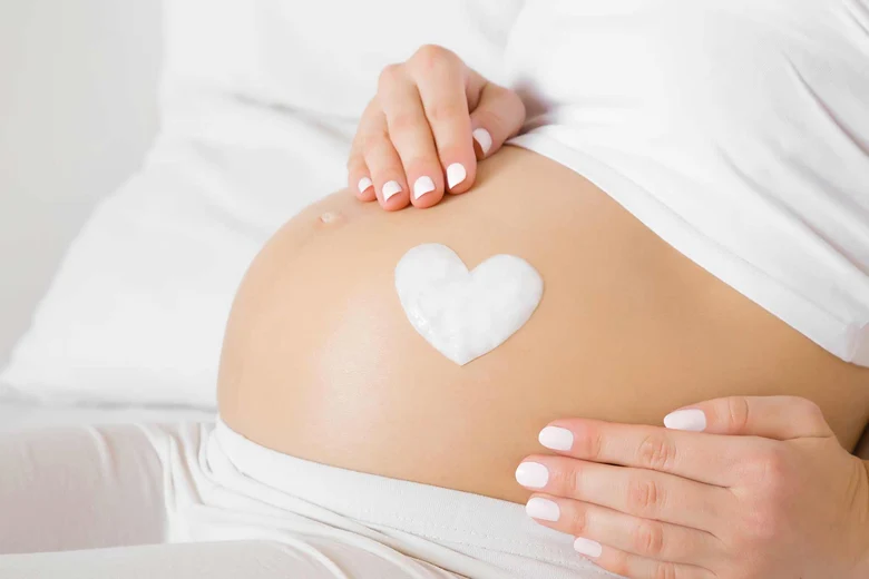 Schwangere Frau. Auf dem Bauch ist ein weißes Herz gelegt