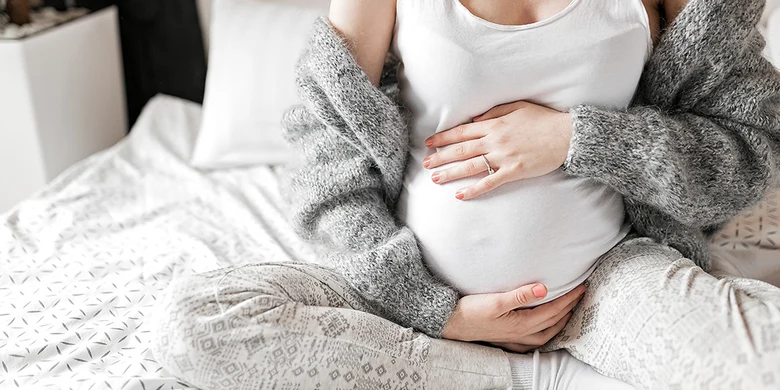 Schwangere Frau sitzt im Bett und hält ihren Bauch