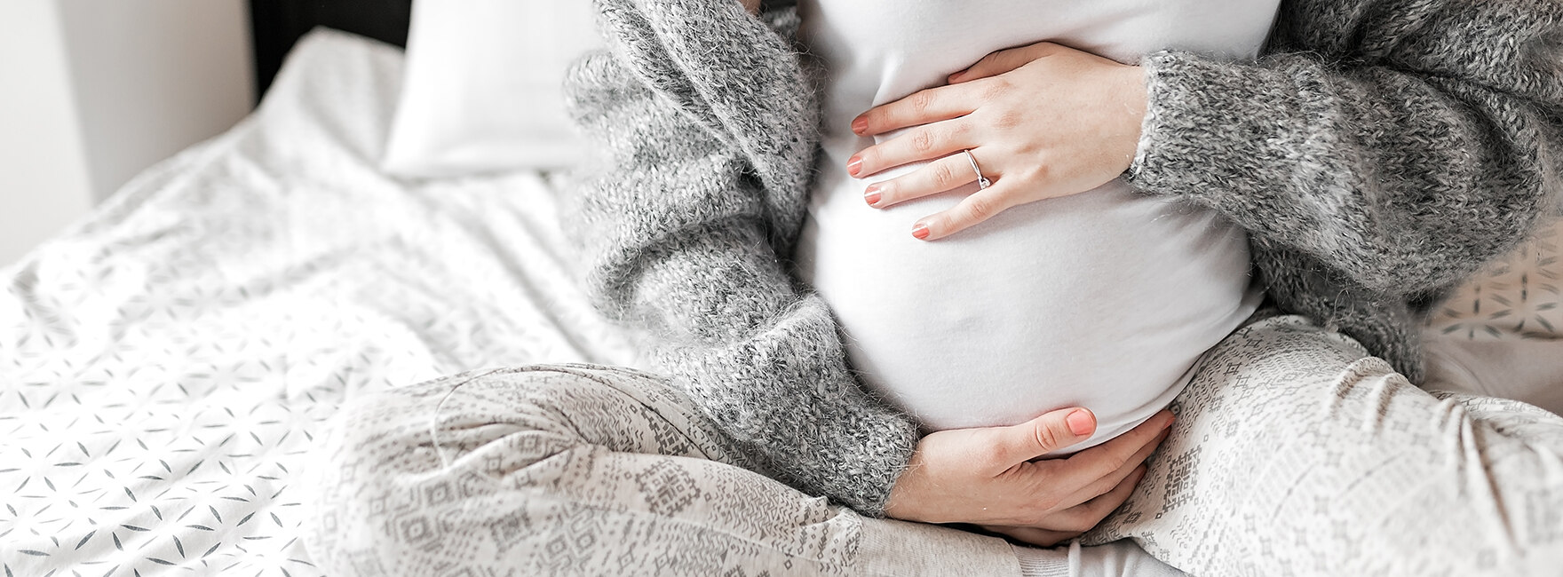 Schwangere Frau sitzt im Bett und hält ihren Bauch