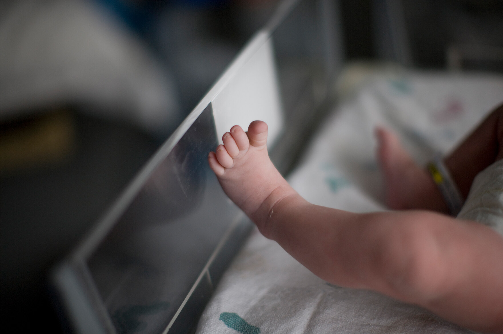 Nackte, strampelnde Beinchen eines Säuglings in einem Neugeborenenbett