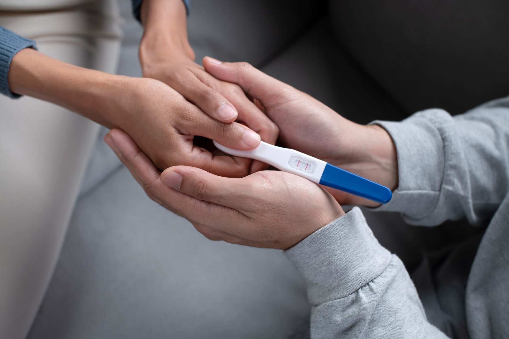 Eine Frauenhand und eine Männerhand halten einen Schwangerschaftstest in der Hand.