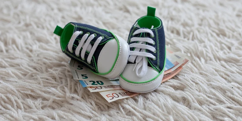 Zwei Kinderschuhe liegen auf Geldscheinen