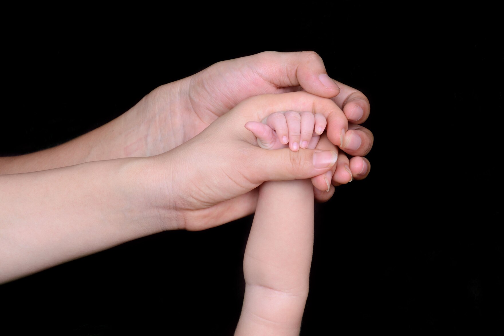 Eine kleine Kinderhand wird von zwei Erwachsenenhänden angefasst