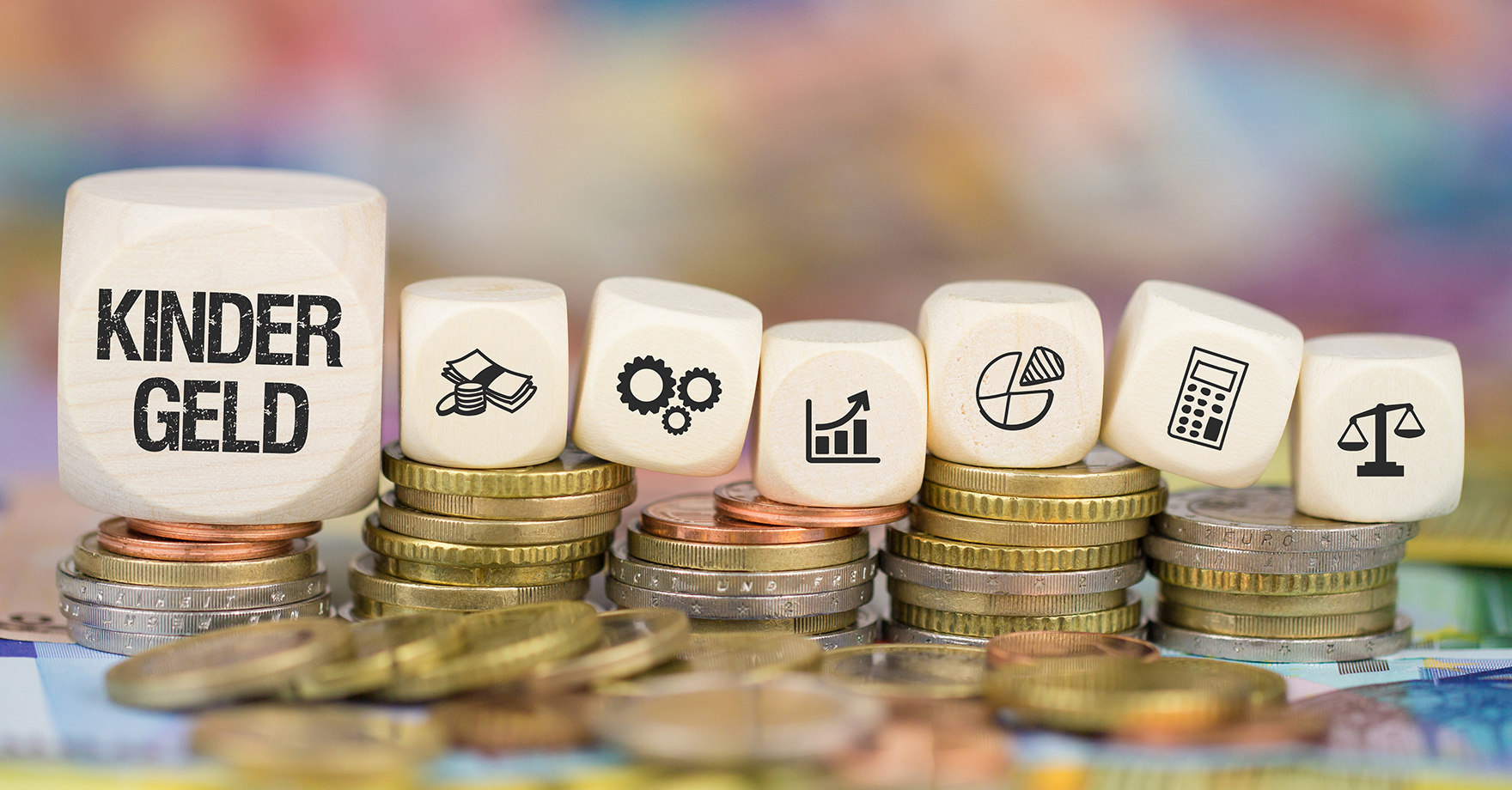 Würfel auf Münzgeldstapeln, der erste Würfel ist beschriftet mit Kindergeld, die anderen sechs Würfel haben Symbole wie Diagramm, Waage, Taschrechner