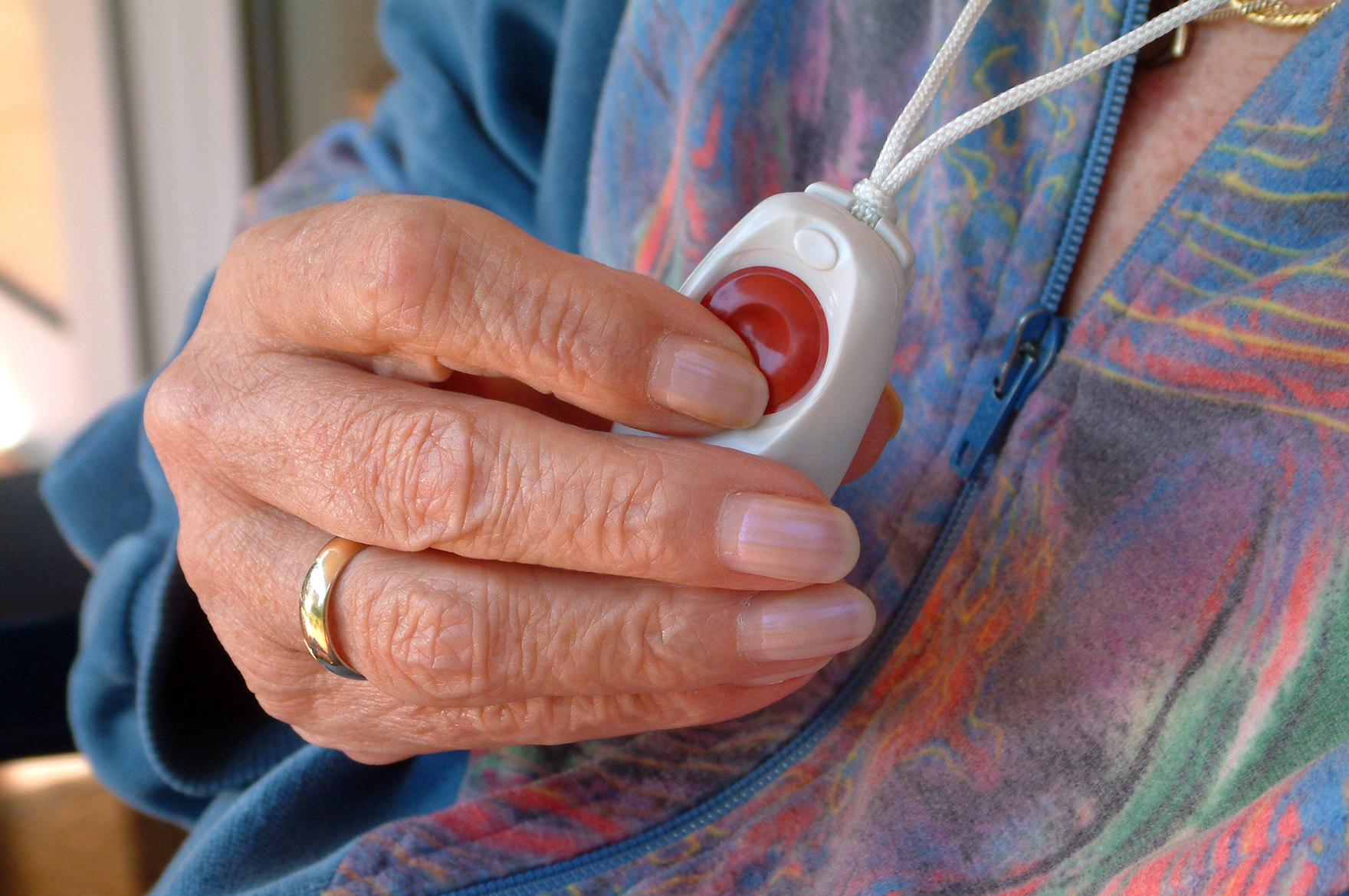 Eine ältere Frau drückt den Knopf des Hausnotrufes, der um ihren Hals hängt.