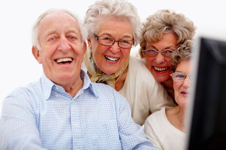 Senioren sitzen lachend vor einem Bildschirm.