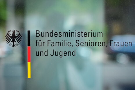 Logo des Bundesministeriums für Familie, Senioren, Frauen und Jugend, fotografiert auf einer Scheibe eines Fensters oder einer Tür