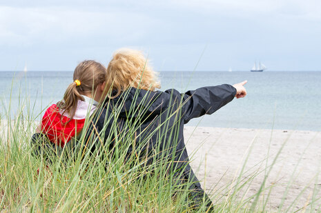 Mutter und Tochter halten sich am Strand im Arm und schauen auf das Meer