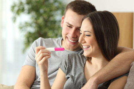 Ein Mann und eine Frau schauen glücklich lächelnd auf einen Schwangerschaftstest.