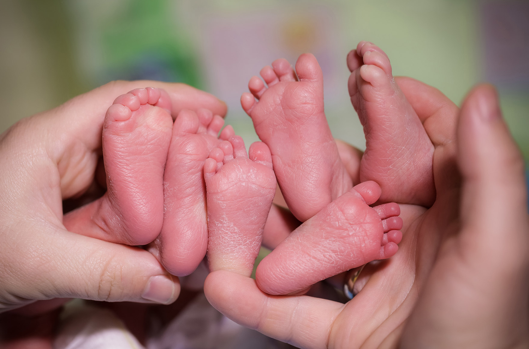 zwei Frauenhände halten sechs nackte Füße von drei Neugeborenen