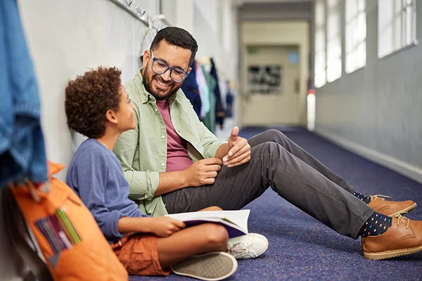 Grundschullehrer hilft dem kleinen Jungen nach dem Unterricht bei den Hausaufgaben