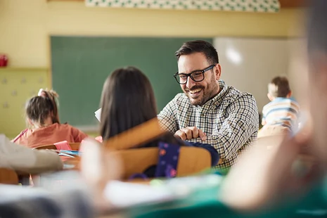 Fröhlicher Lehrer in der Schule hilft Schülerin und lächelt