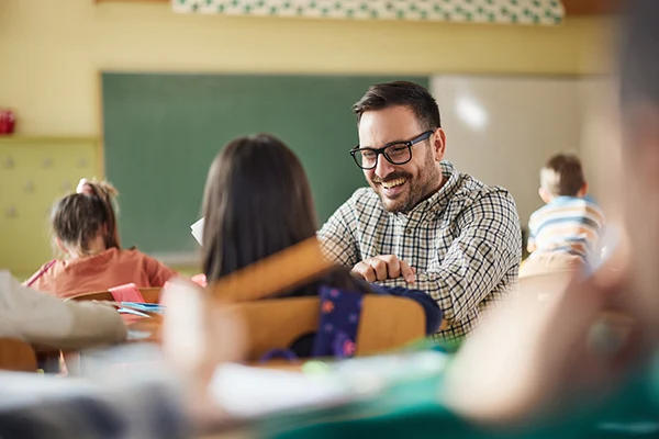 Fröhlicher Lehrer in der Schule hilft Schülerin und lächelt
