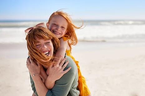 Fröhliche junge Mutter lächelt mit kleiner Tochter am Strand
