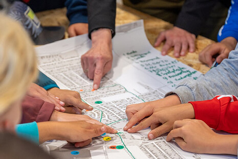Kinder zeigen mit den Fingern auf eine Karte, die auf einem Tisch liegt.
